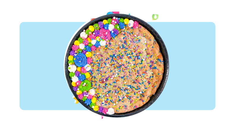 A cookie cake with colored sprinkles, confetti and frosting in front of a background.