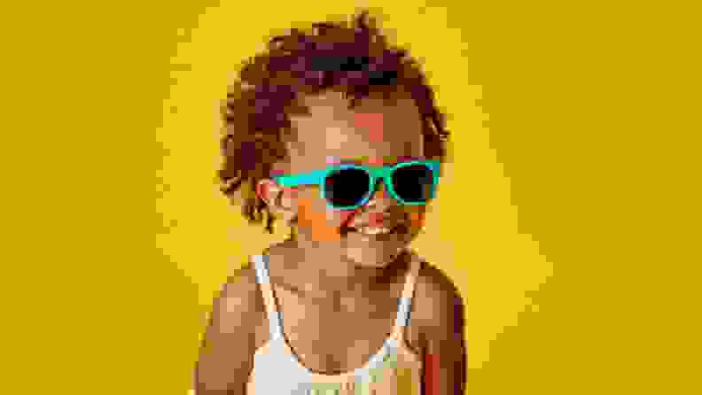 An adorable Black girl smiles at the camera in her teal sunglasses
