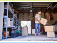 Person standing in garage while holding moving boxes indoors.