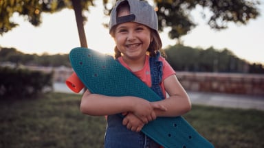 A girl smiles as she hugs her Penny Board beginner skateboard for kids.