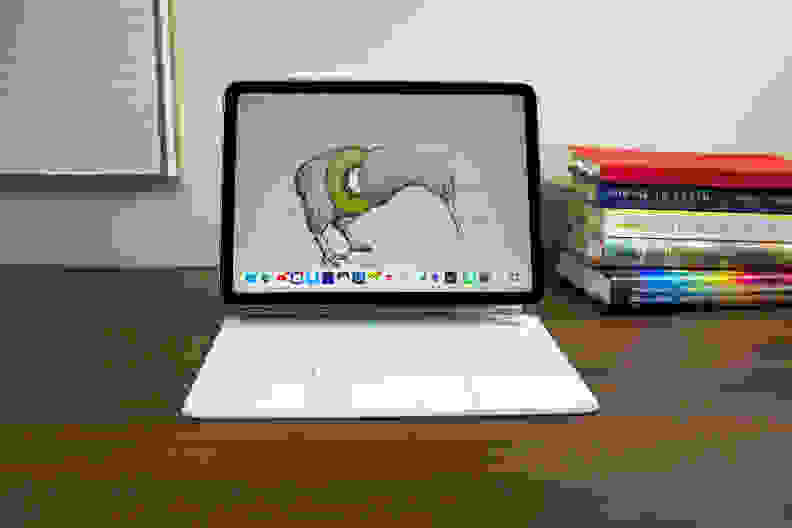 The M1 iPad Air attached to Apple's Magic Keyboard, with the screen on showing a wallpaper of a kiwi bird, with books and art in the background.