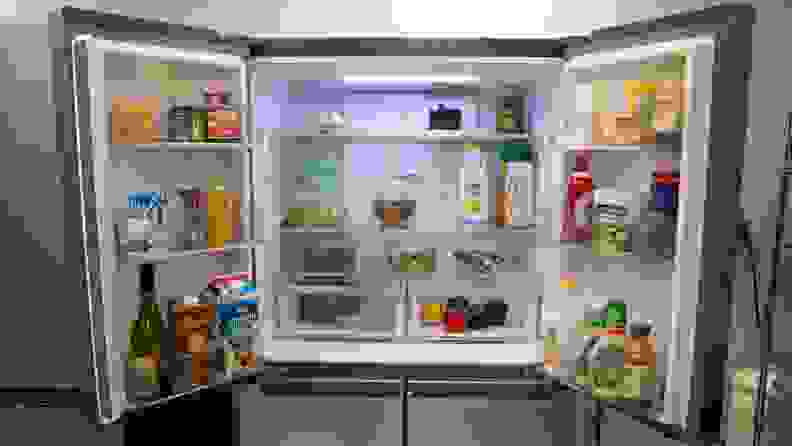 A close-up of the fridge compartment. Both of its doors are open and its shelves and bins are stocked with food.