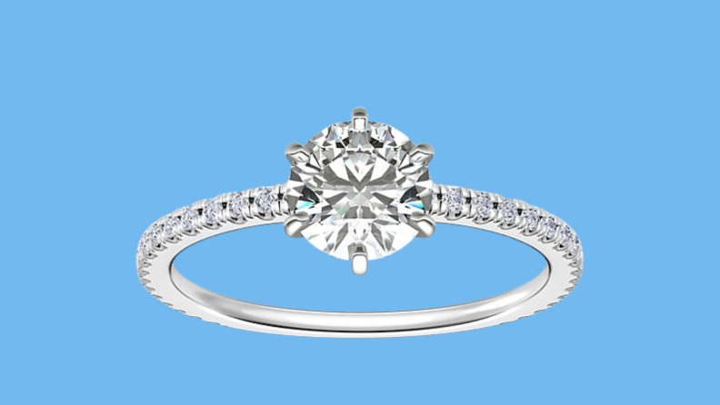 An image of a white gold ring with a round diamond and a diamond-studded band.
