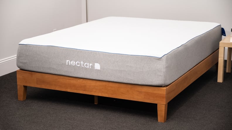 A bare Nectar mattress on a wood bed frame in a carpeted room with white walls