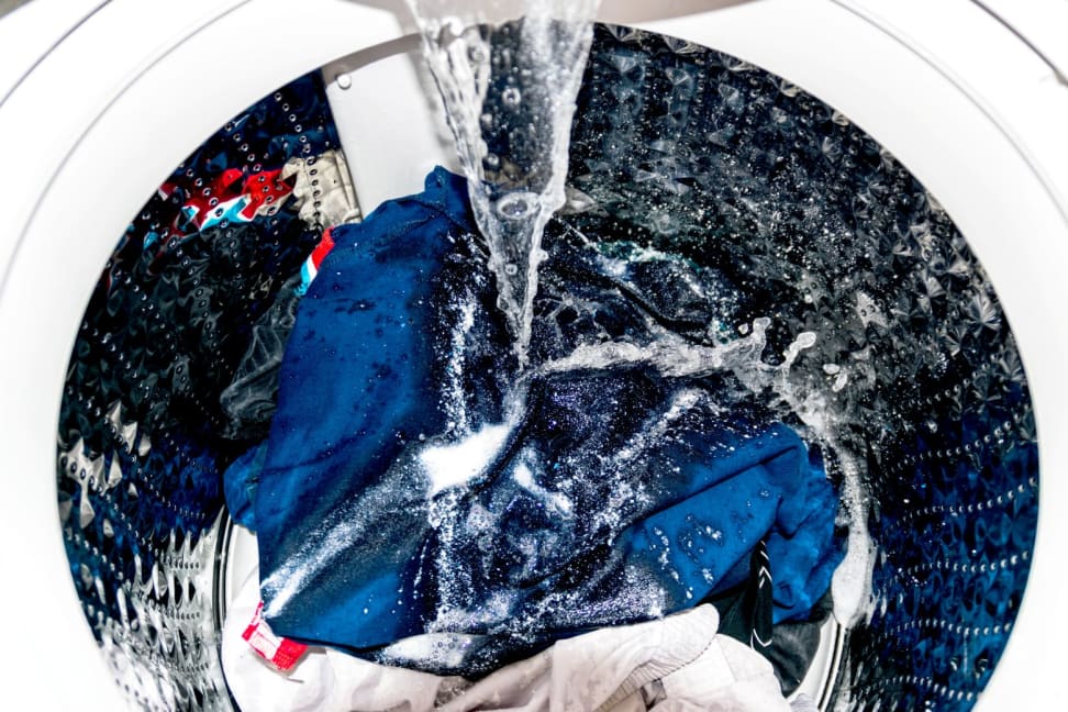 A washing machine being filled with water, with some clothing and powder detergent inside