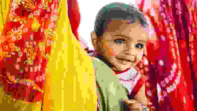 An Indian child smiles surrounded by colorful fabrics