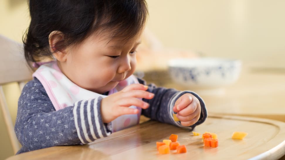 baby girl sitting in a high chair eating food with her hands