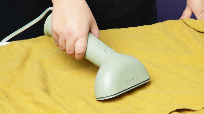 A person using the Steamery Cirrus 3 as an iron on a green linen shirt.