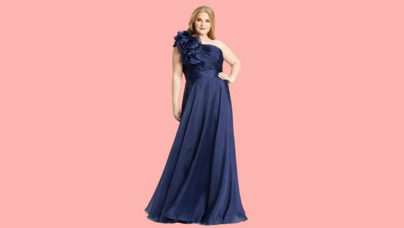 A model wearing a navy formal gown with a ruffle detail at the shoulder.