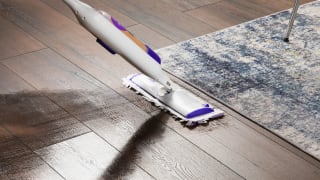 The Swiffer PowerMop, mopping a wood floor next to an area rug.