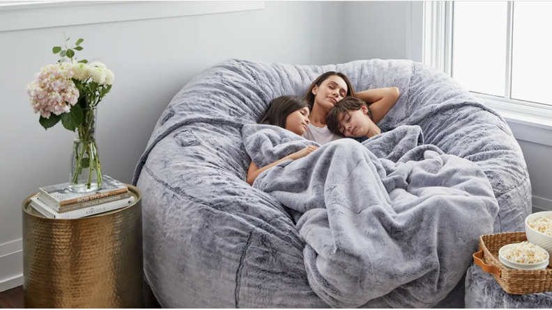 Woman and two children sleeping together under blanket on top of Lovesac bean bag.