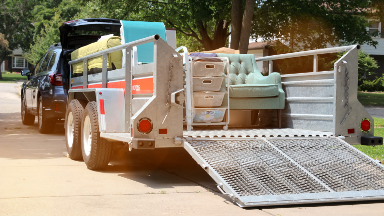 A car with a moving trailer filled with household items.