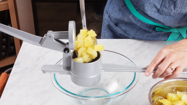 Cubed potatoes in a potato ricer over a glass bowl