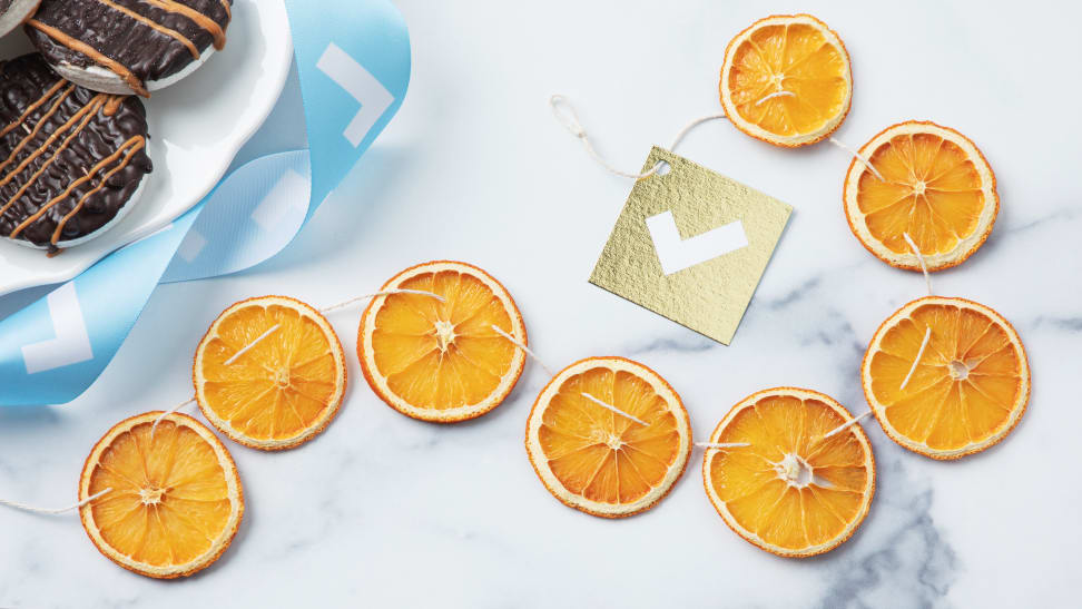 A string of dried orange garland on a table with cookies and gift wrapping.