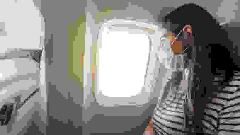 A person sitting on an airplane wearing a face mask and looking out the window.
