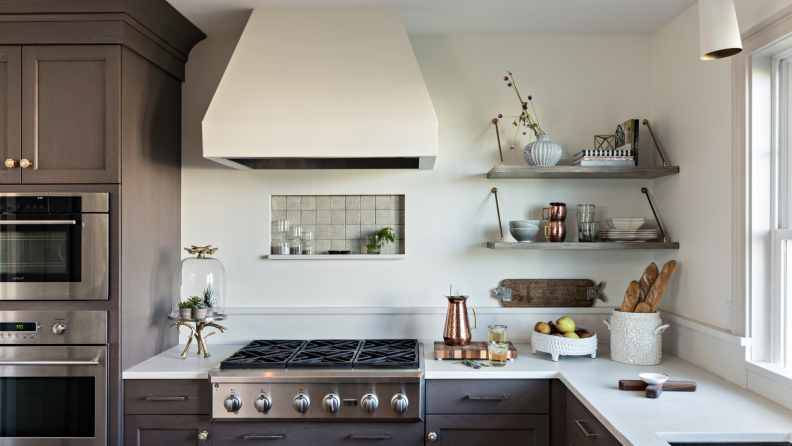 A simplistic kitchen with a white range hood over a stainless steel stove and oven.