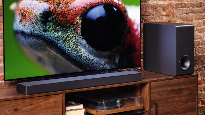 An lg S80QY soundbar sits on a TV stand next to a television set.