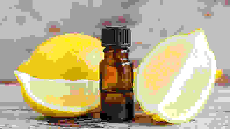 A shot of two quartered lemons sitting next to a small amber vial of lemon oil.