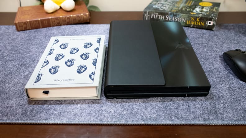 Zenbook Fold 17 OLED closed next to hardcover book on tabletop.