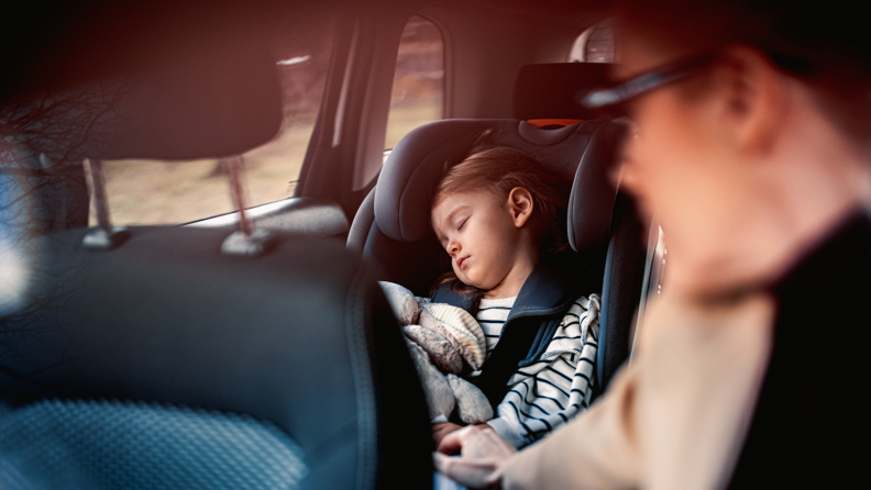 Cute girl napping with her toy in child safety seat while her unrecognizable mother driving car.