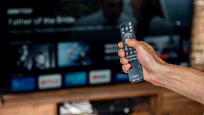 Shot of a hand holding up the new standard Sony remote in front of the Sony X95K LED TV.