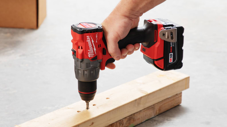 A person using the Milwaukee M18 Cordless Hammer Drill to drill a nail into a slim wood panel.