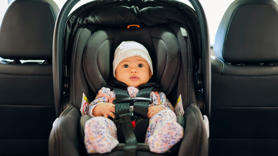 A 3-month-old baby sitting in a car seat in the backseat of a vehicle.