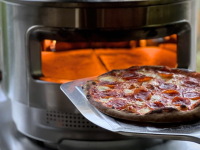 Person using metal pizza peel to take small pepperoni pizza out of Solo Stove Pizza Oven.