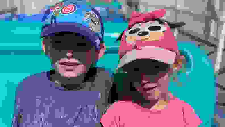 A young boy wearing a Toy Story baseball cap sitting next to a young girl wearing a pink mini mouse hat
