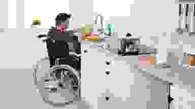 A man in a wheelchair, pulled up to a wheelchair-friendly kitchen sink, washing dishes.