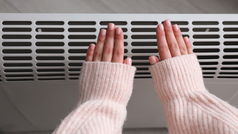 Person holding hands up to space heater for warmth.