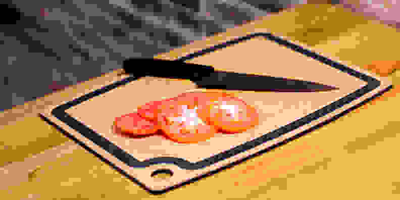 A knife and some slices of tomatoes on a wooden cutting board.