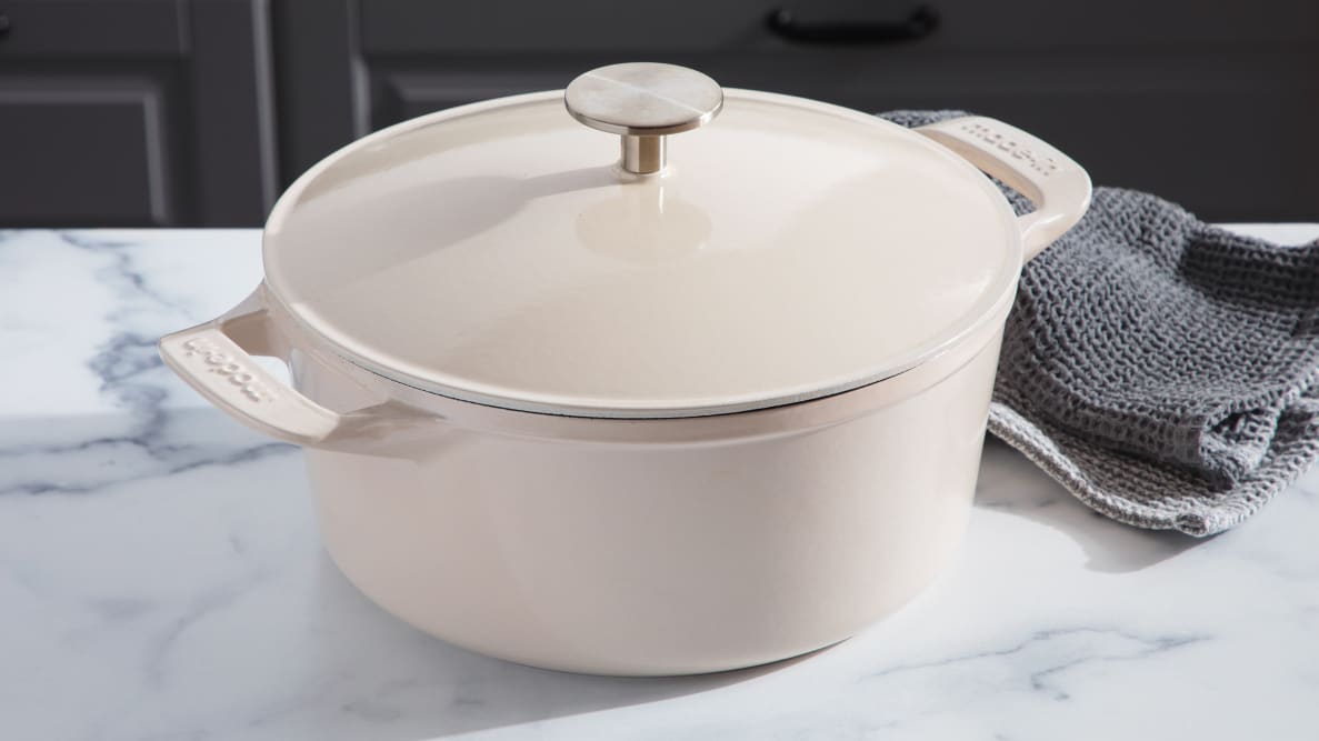 Product shot of the cream colored Made In Dutch Oven with lid on top of granite countertop next to gray dishcloths.