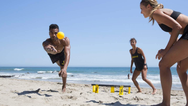 A person dives during a spikeball game on a beach.