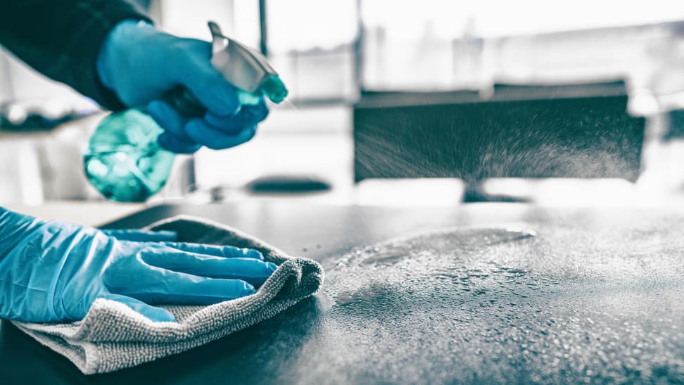 有喷洒在与清洁解答的一张桌的蓝色手套的手在薄雾瓶