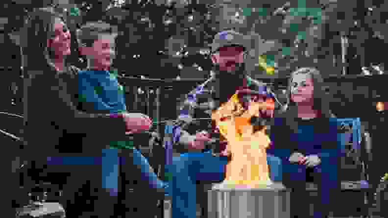 Four people gather around a portable fire pit.