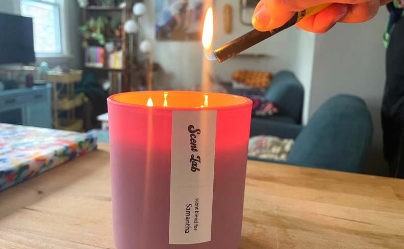 A person using a lighter to light a personalized, pink, Scent Lab candle.