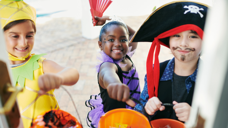 Three children in Halloween costumes hold out their candy buckets to door at residential home.