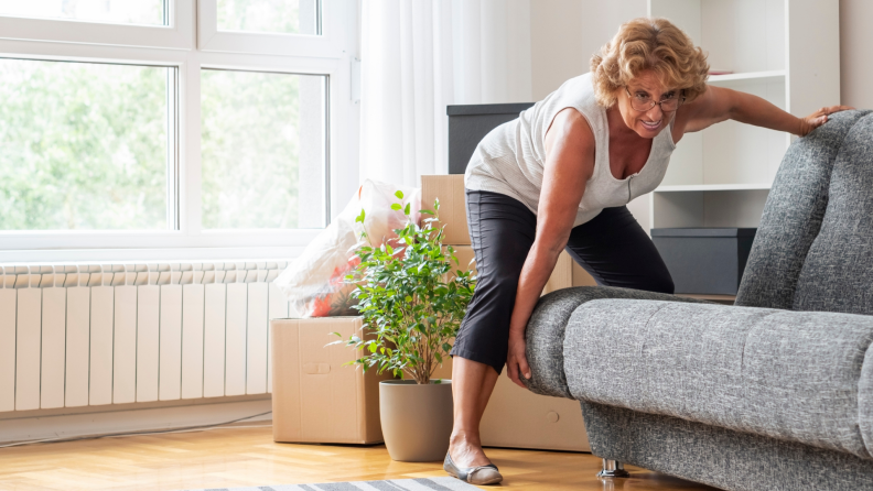 Senior woman moving couch in new living space.