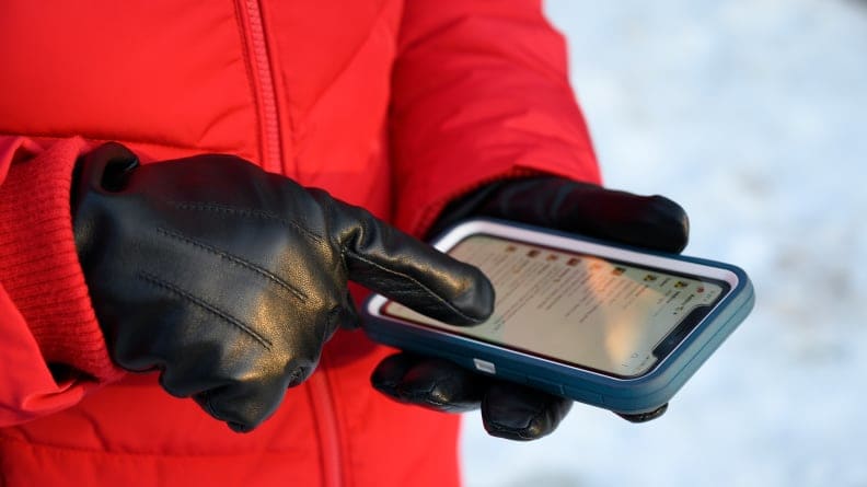 A person uses their smartphone while wearing black leather gloves in the wintertime.