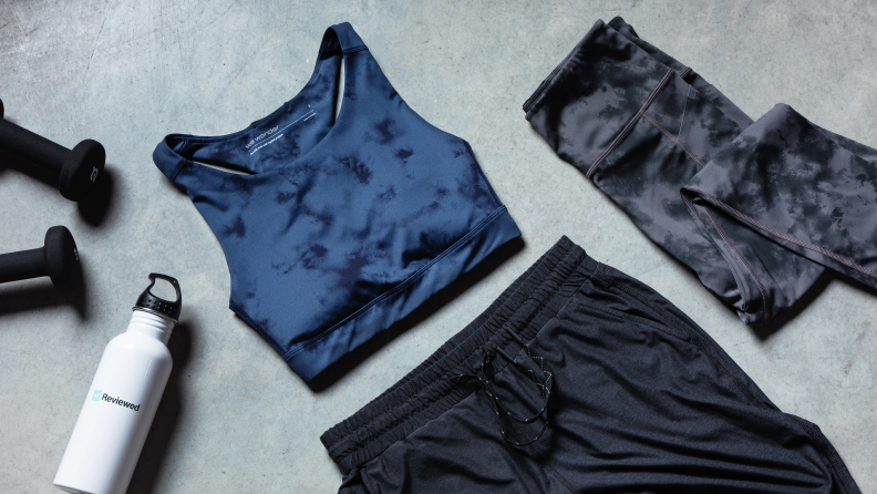 A sports bra, joggers, and running shorts surrounded by a water bottle and weights.