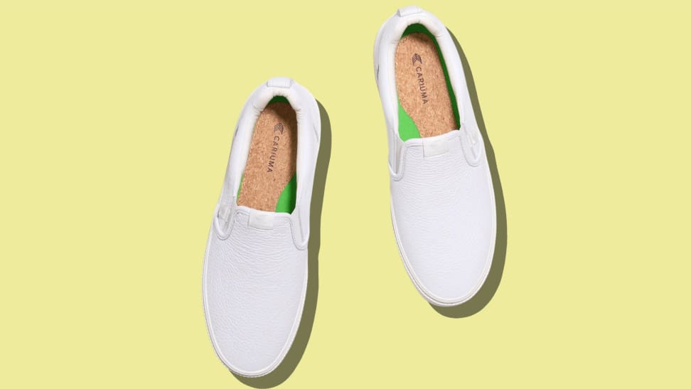 White Cariuma slip-on leather shoes with a yellow background. You can see their cork insoles from this angle.