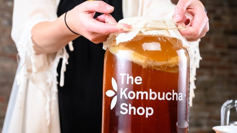 A person wraps a jug of Kombucha with cheese cloth.