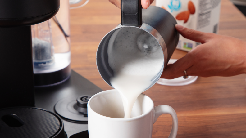 Close view of creamy foam being poured from the K-Cafe Smart's milk milk frother into a coffee mug.