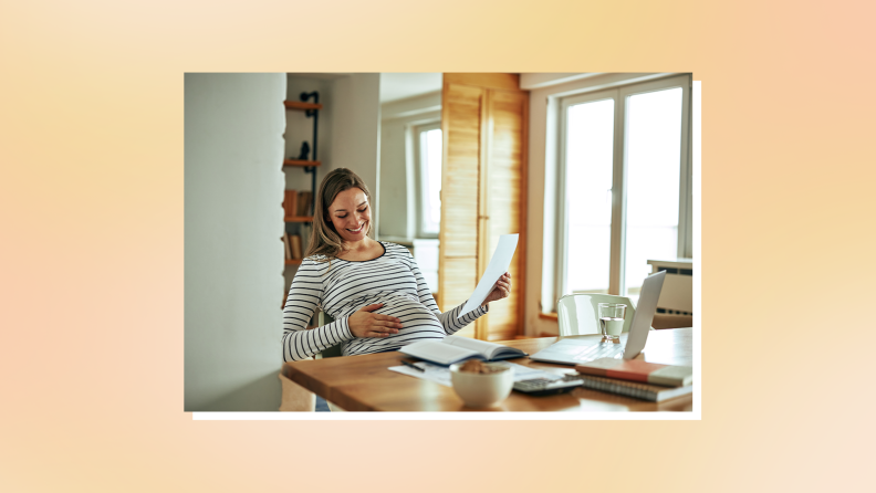 Pregnant person sitting at table indoors while reviewing documents.