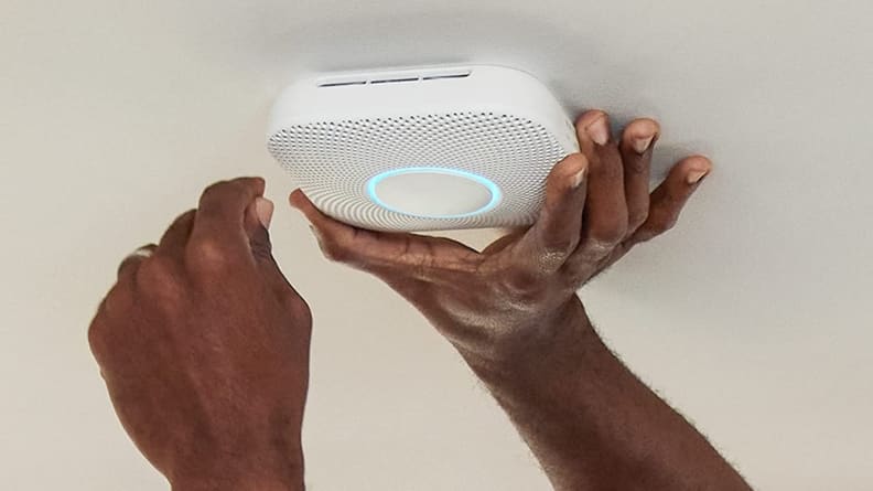 Person using hands to install smart smoke detector on wall.