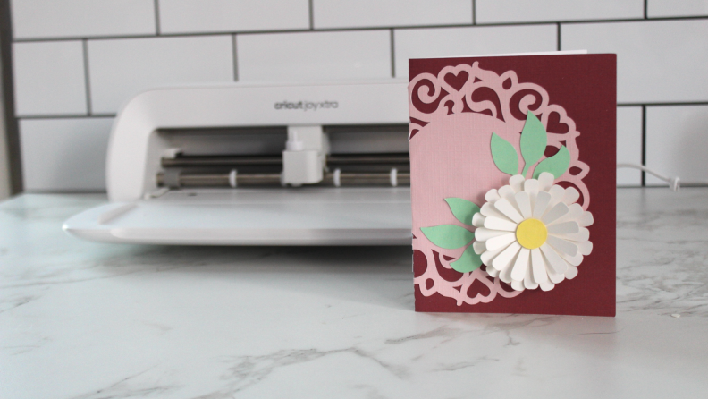 An intricate handmade card in front of the Cricut Joy Xtra.