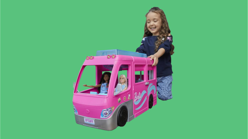 Dziewczynka bawiąca się różową Barbie Camper z dwiema lalkami Barbie na przednim siedzeniu.