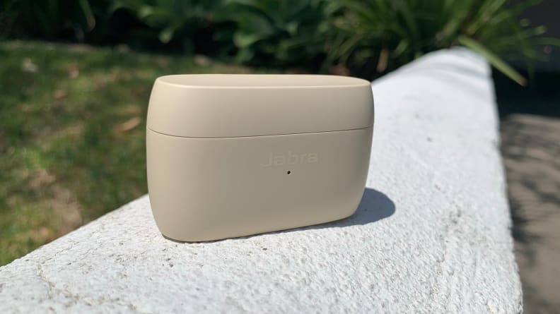The gold beige charging case for the Jabra Elite 5 sits on a white stone wall.