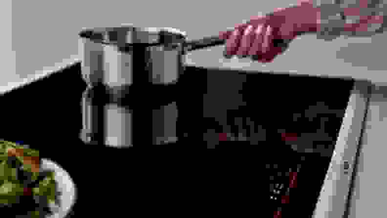 A lifestyle image of a person gripping the handle of a pan on an induction oven.